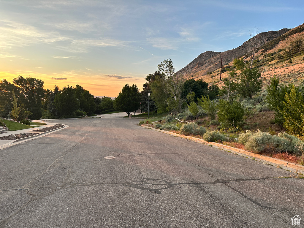 View of asphalt road featuring a mountain view, street lighting, and curbs
