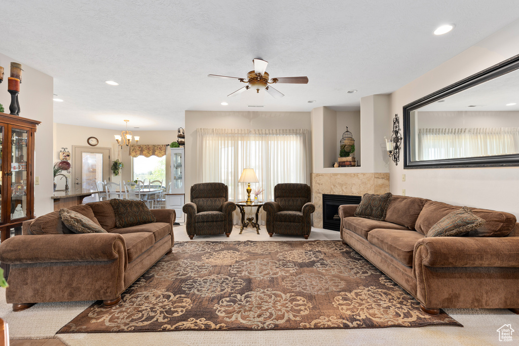Carpeted living room featuring a ceiling fan, a chandelier, a tiled fireplace, and recessed lighting