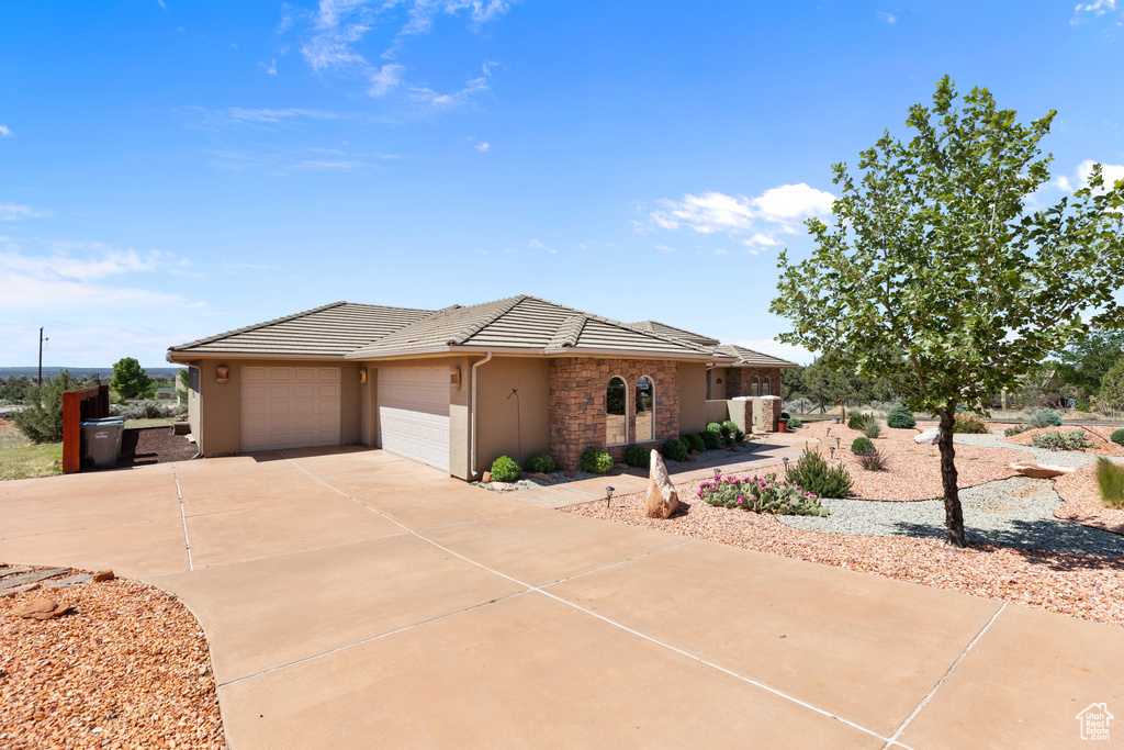 View of front facade featuring a tiled roof, stucco siding, an attached garage, concrete driveway, and stone siding