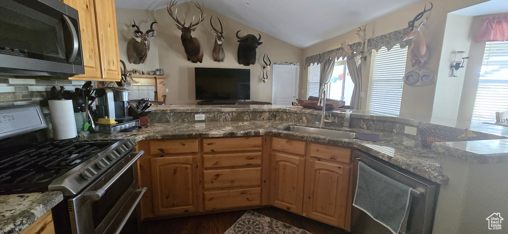 Kitchen featuring appliances with stainless steel finishes, healthy amount of natural light, dark stone countertops, vaulted ceiling, and open floor plan