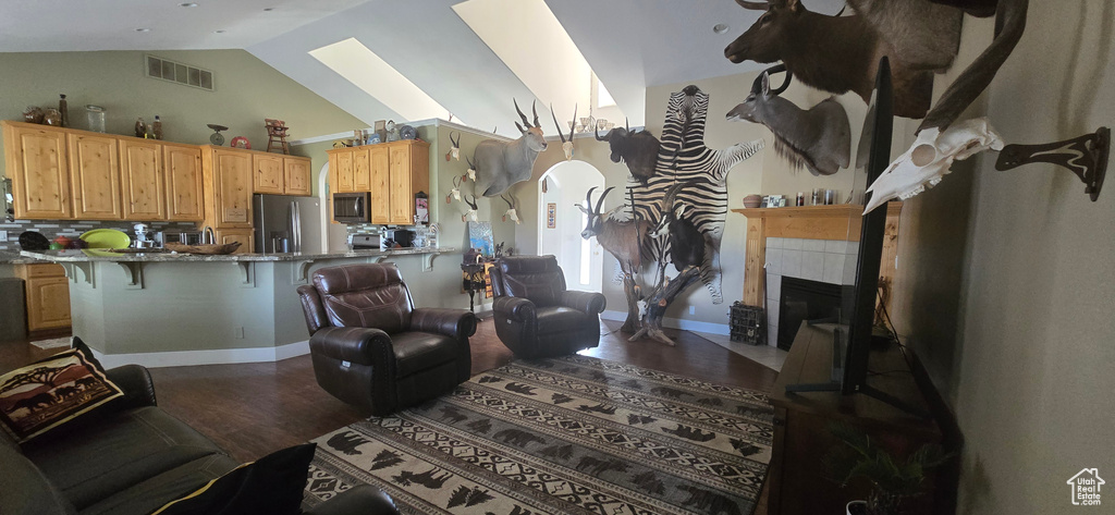 Living area with wood finished floors, vaulted ceiling, a tiled fireplace, and a skylight