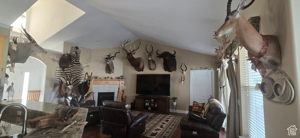 Living area featuring a tiled fireplace, wood finished floors, vaulted ceiling, and arched walkways
