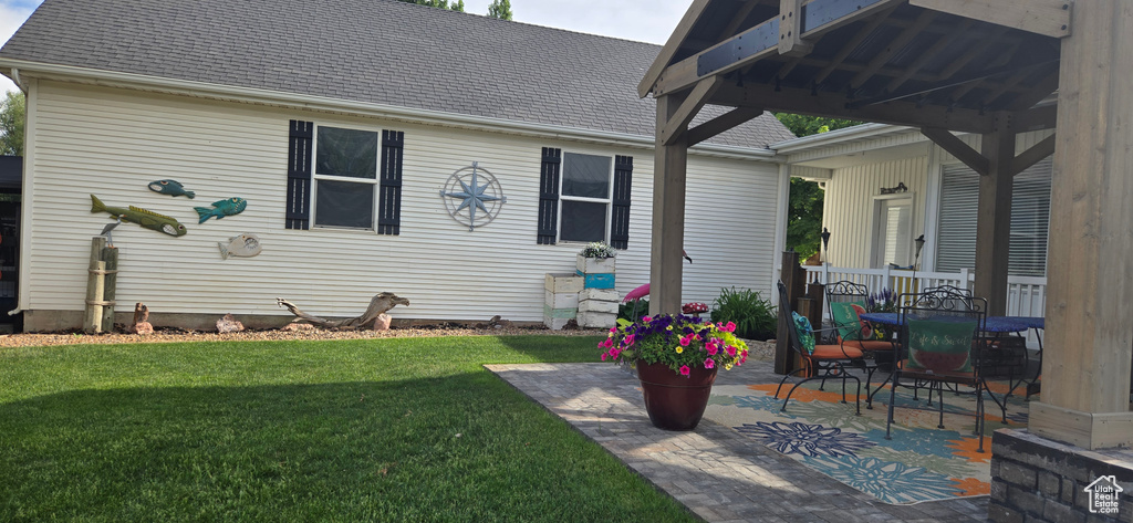 Back of property featuring a lawn, roof with shingles, and a patio area
