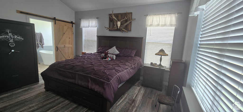 Bedroom with a barn door, wood finished floors, vaulted ceiling, and ensuite bath