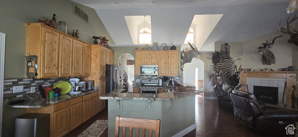 Kitchen featuring appliances with stainless steel finishes, stone countertops, tasteful backsplash, arched walkways, and a kitchen breakfast bar