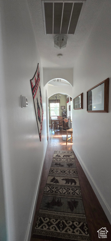 Corridor featuring arched walkways, dark wood-style floors, and baseboards