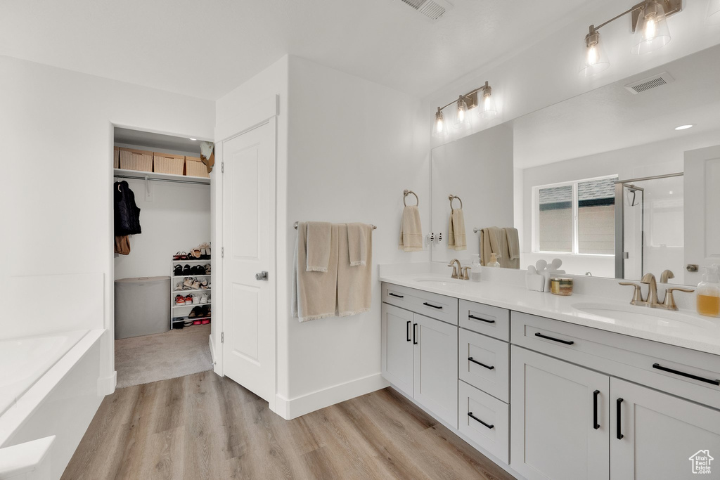 Bathroom featuring wood finished floors, double vanity, a stall shower, a garden tub, and a spacious closet