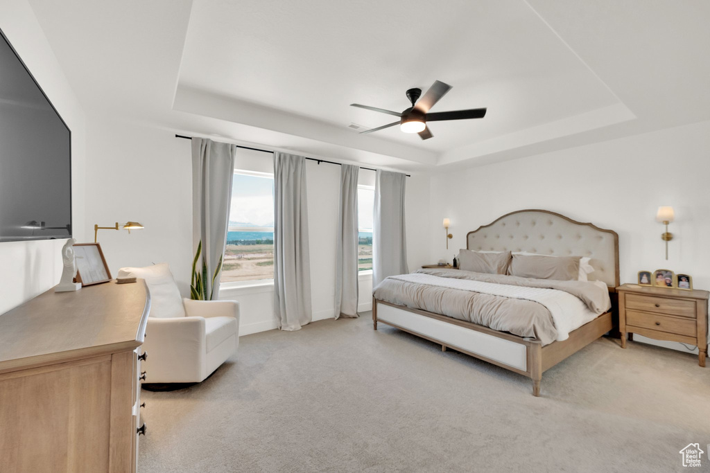 Bedroom featuring a tray ceiling, light colored carpet, and ceiling fan