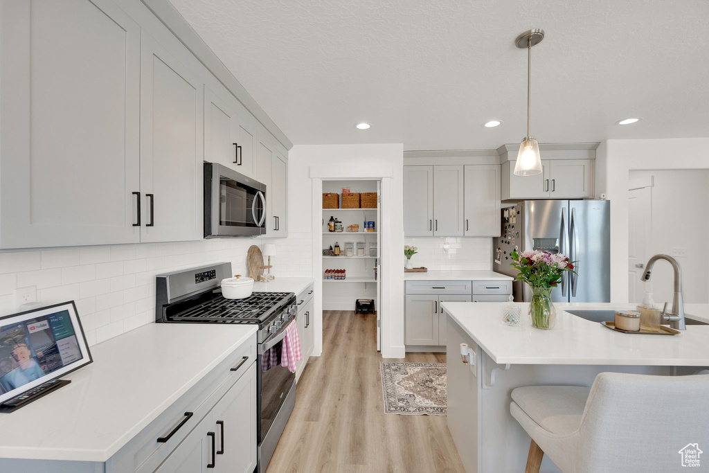Kitchen with appliances with stainless steel finishes, light wood-style floors, hanging light fixtures, a sink, and a kitchen bar