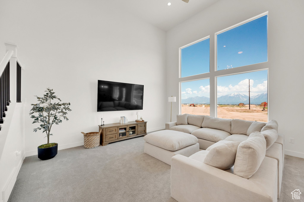 Living area with a high ceiling, light carpet, baseboards, a ceiling fan, and stairway