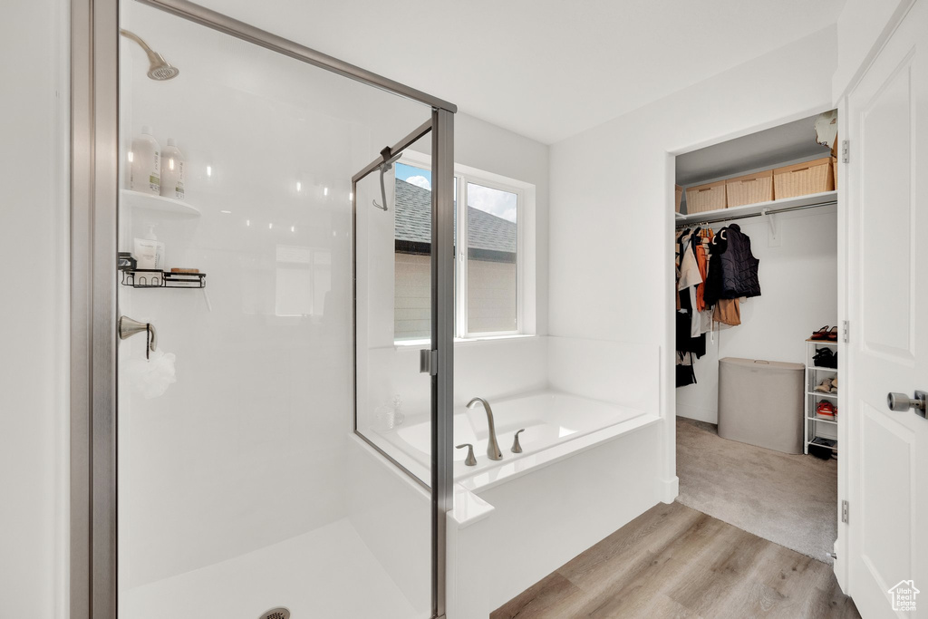 Bathroom with a stall shower, a garden tub, a walk in closet, and wood finished floors