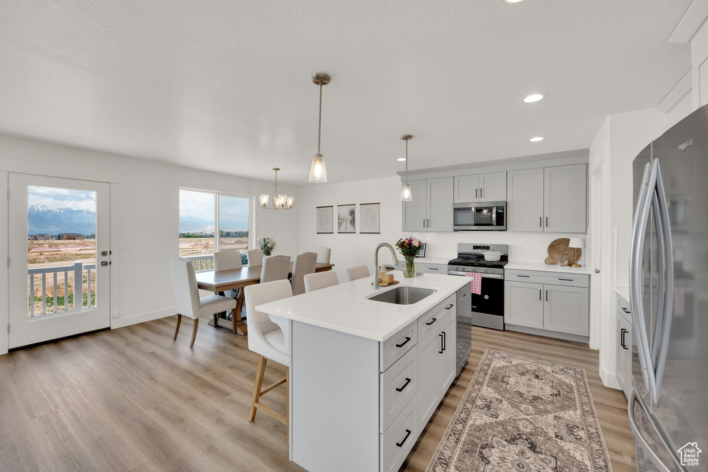 Kitchen with stainless steel appliances, a sink, a kitchen breakfast bar, light wood-style flooring, and light countertops