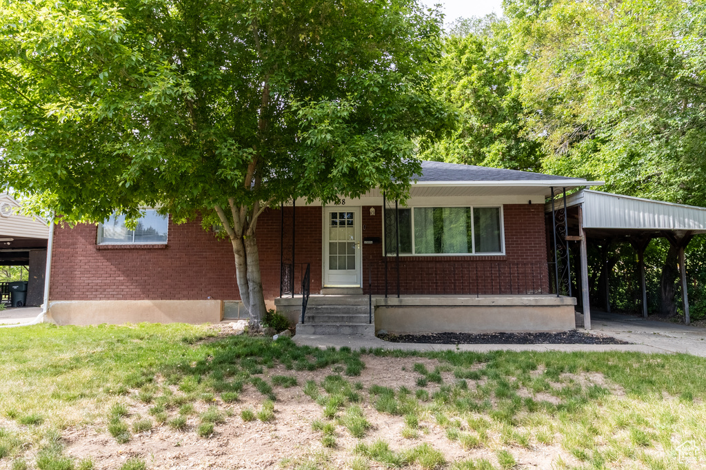 View of front of home with brick siding, a carport, and a front lawn