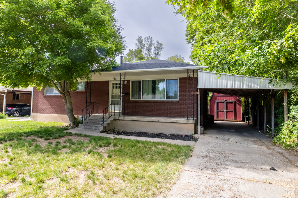 View of front of property featuring brick siding, driveway, a carport, and an outbuilding