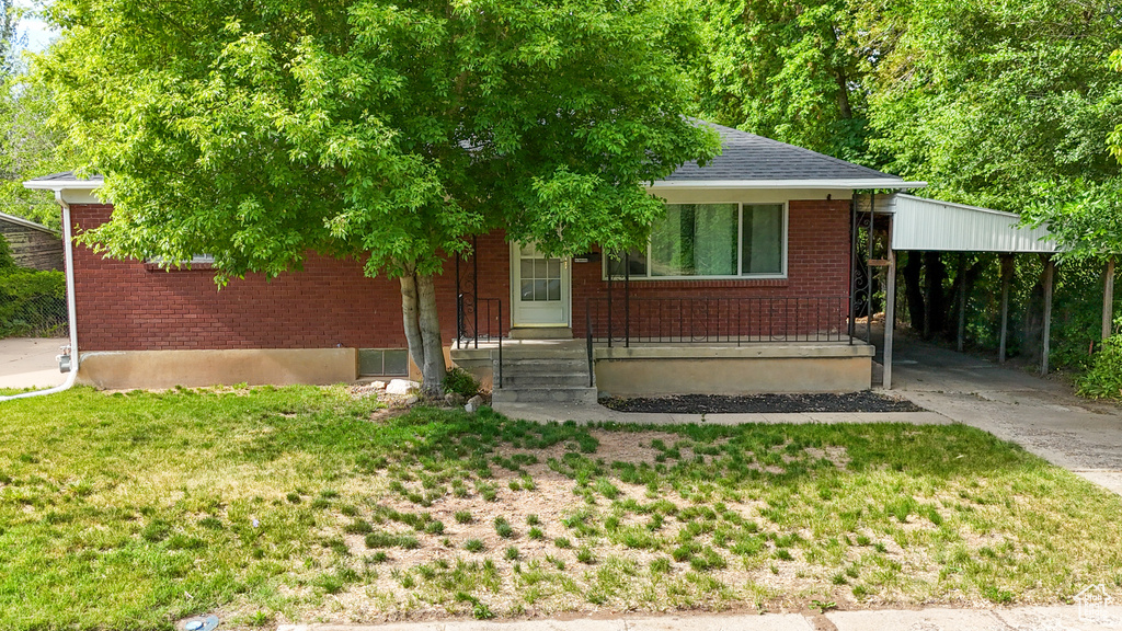 Bungalow-style home with brick siding, a carport, a front lawn, and roof with shingles