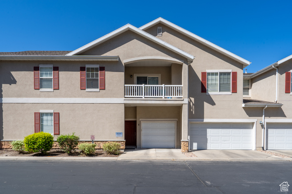 Townhome / multi-family property featuring stucco siding, an attached garage, a balcony, and driveway