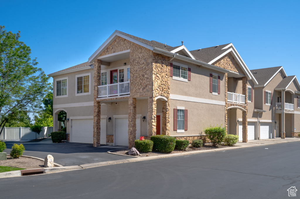 Multi unit property featuring stone siding, a balcony, stucco siding, and a garage