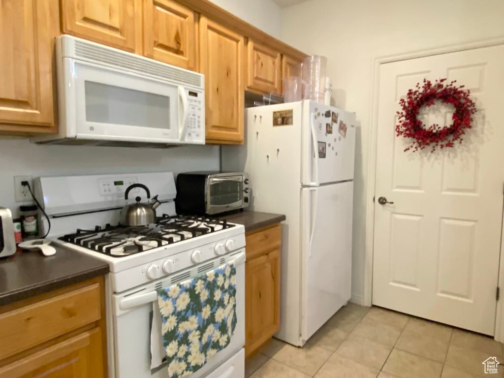Kitchen with white appliances, dark countertops, and light tile patterned floors