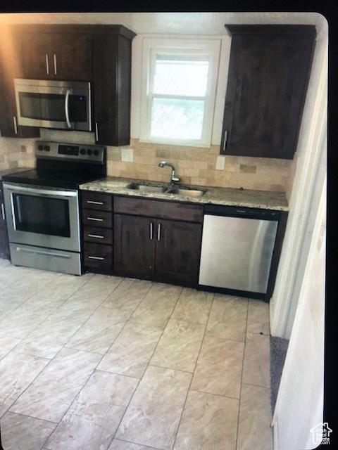 Kitchen with stainless steel appliances, a sink, backsplash, and dark brown cabinetry