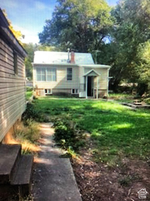 Back of house featuring a chimney and a lawn