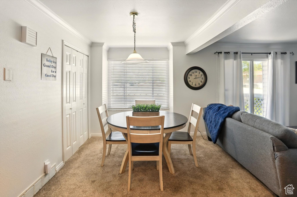 Dining room with ornamental molding, light colored carpet, and baseboards