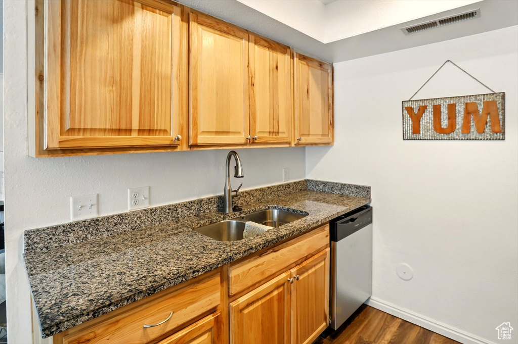Kitchen featuring dishwasher, a sink, dark wood-style floors, dark stone counters, and baseboards