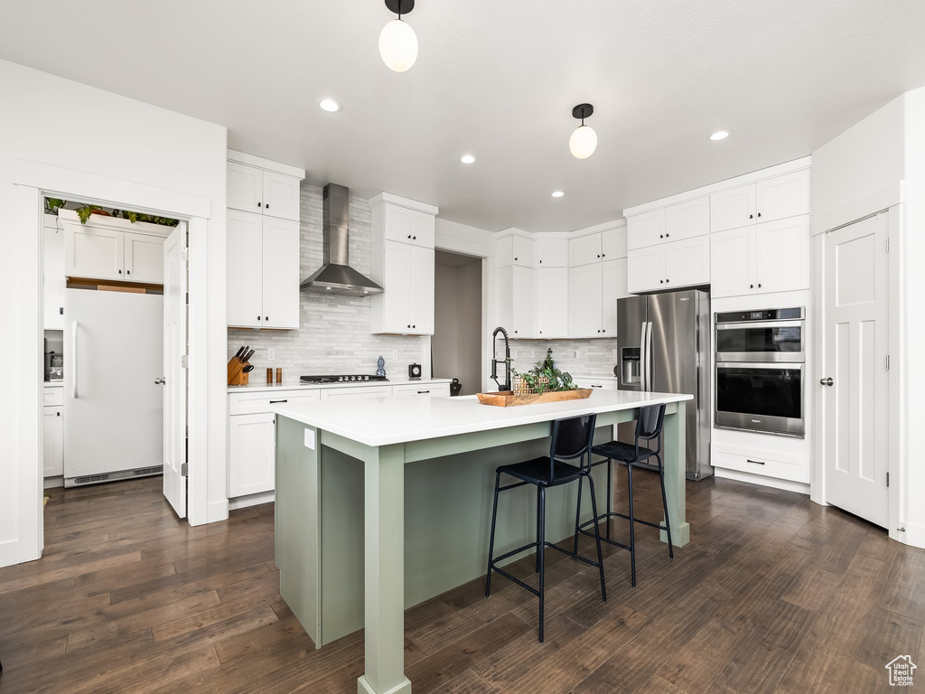 Kitchen with stainless steel appliances, wall chimney exhaust hood, light countertops, backsplash, and recessed lighting