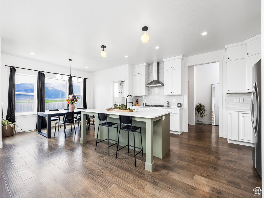Kitchen featuring wall chimney exhaust hood, decorative backsplash, light countertops, a breakfast bar area, and recessed lighting