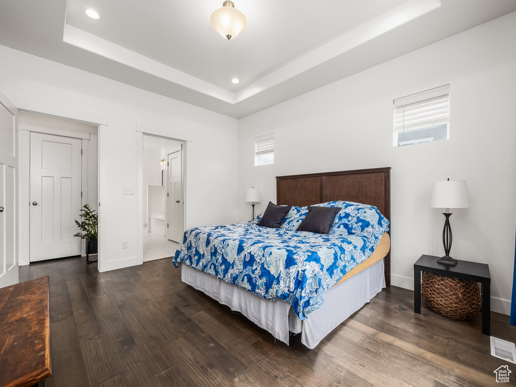 Bedroom with wood finished floors, a tray ceiling, recessed lighting, baseboards, and ensuite bath
