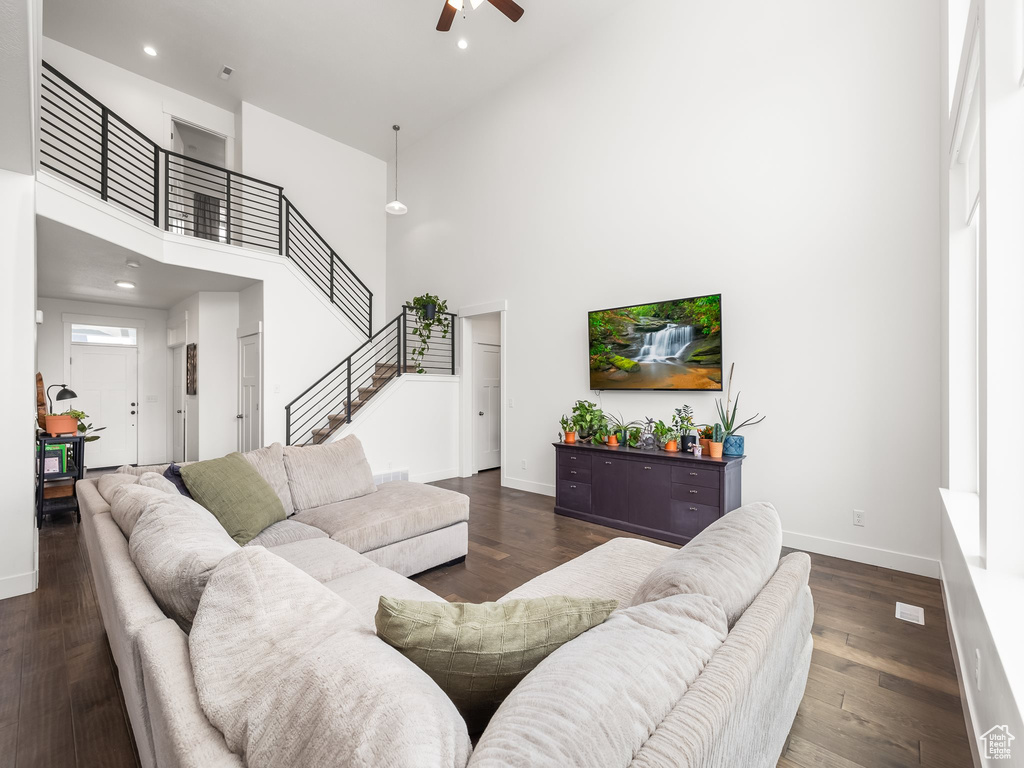 Living room featuring a high ceiling, a ceiling fan, stairway, baseboards, and dark wood finished floors