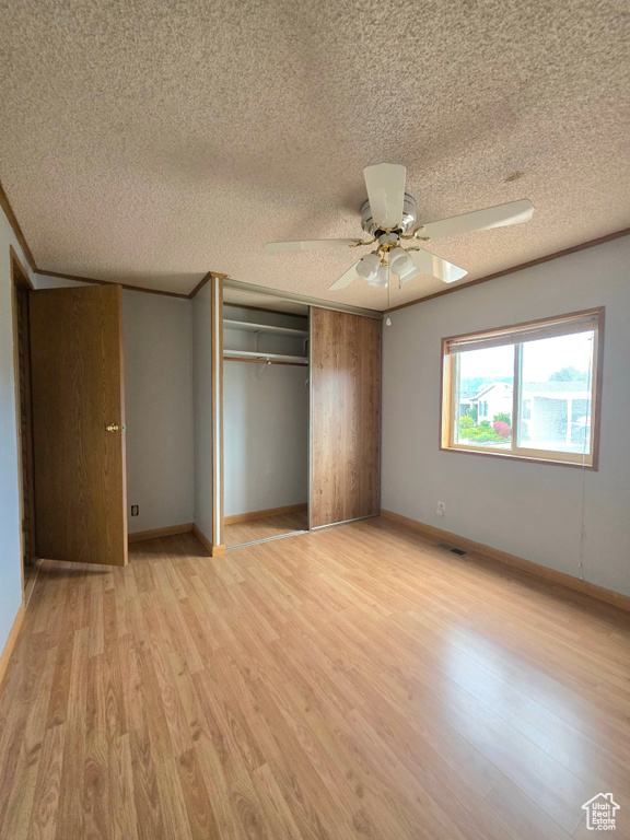 Unfurnished bedroom featuring a textured ceiling, light wood-style floors, a closet, ceiling fan, and baseboards