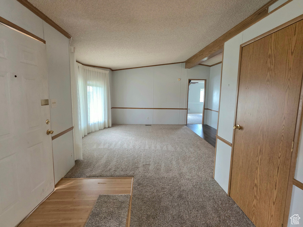 Empty room with a textured ceiling, wood finished floors, crown molding, beamed ceiling, and carpet flooring