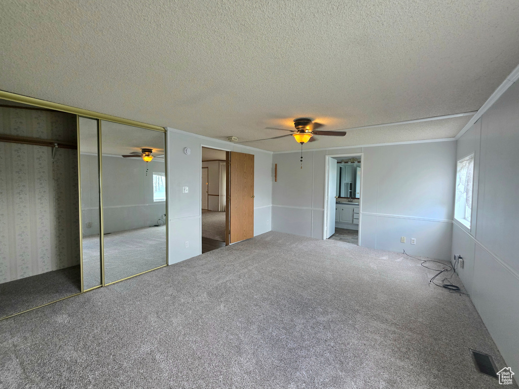 Unfurnished bedroom featuring a textured ceiling, multiple windows, carpet floors, and a ceiling fan