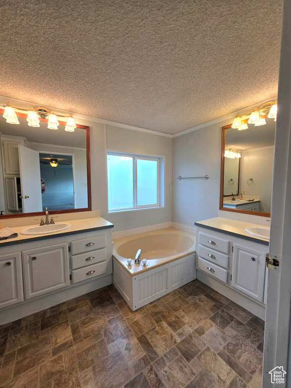 Full bath with two vanities, stone finish floors, a garden tub, crown molding, and a textured ceiling