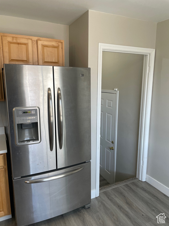 Kitchen view of stainless steel fridge with ice dispenser, wood finished floors, baseboards, and light brown cabinets
