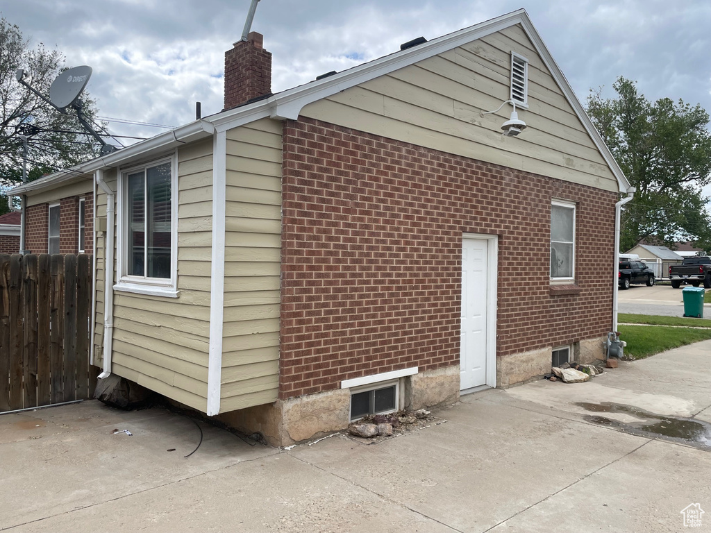 View of property exterior with a chimney, brick siding, and a patio
