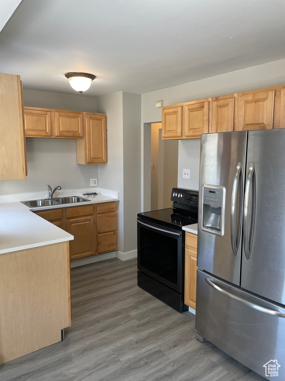 Kitchen with stainless steel fridge with ice dispenser, black range with electric stovetop, a sink, and wood finished floors