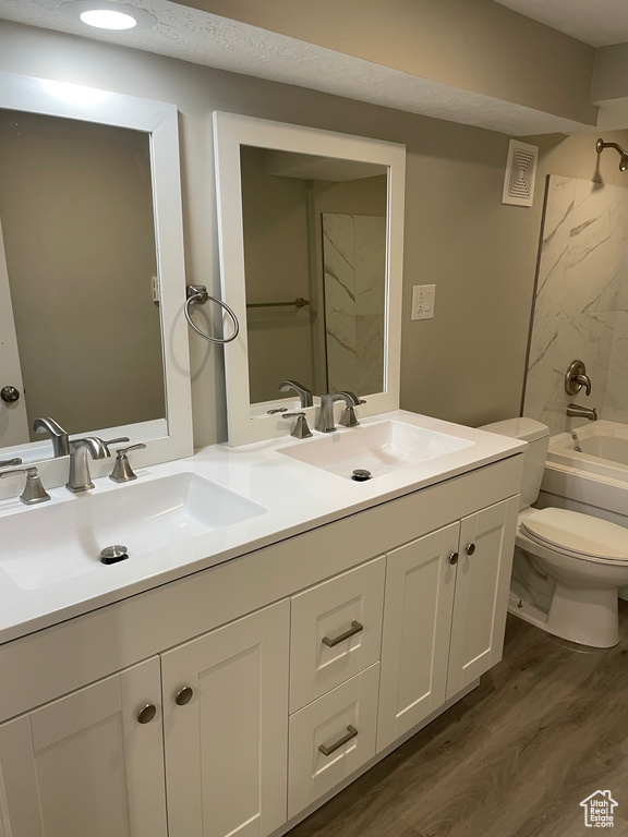 Bathroom with double vanity, wood finished floors, toilet, and shower / bathtub combination