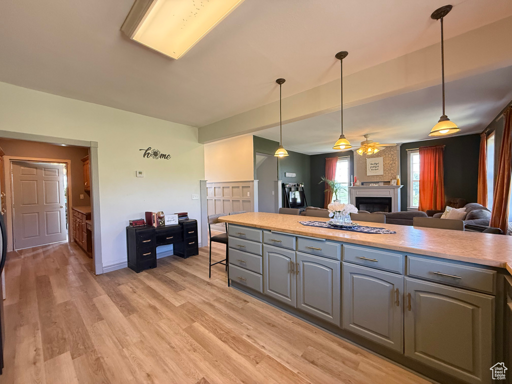 Kitchen with gray cabinetry, a fireplace, open floor plan, light wood finished floors, and light countertops