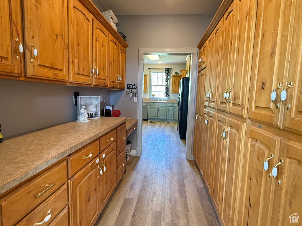 Kitchen featuring brown cabinets, light wood-style flooring, light countertops, stainless steel dishwasher, and freestanding refrigerator