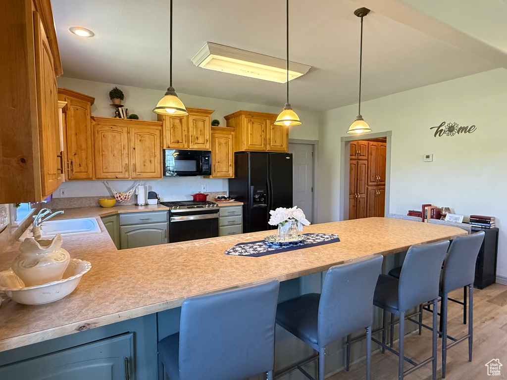 Kitchen featuring black appliances, a sink, a peninsula, light countertops, and hanging light fixtures