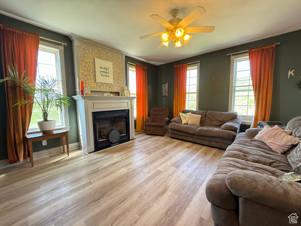 Living area featuring a large fireplace, a ceiling fan, light wood finished floors, and baseboards