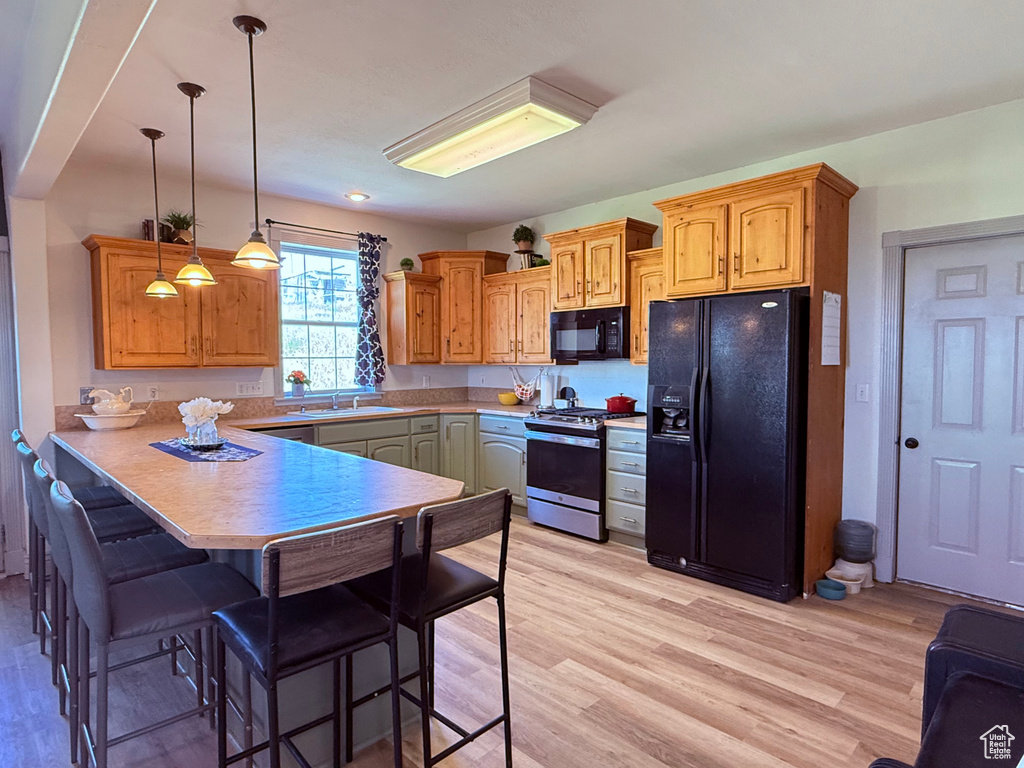 Kitchen with black appliances, a peninsula, a kitchen breakfast bar, light wood-style floors, and pendant lighting