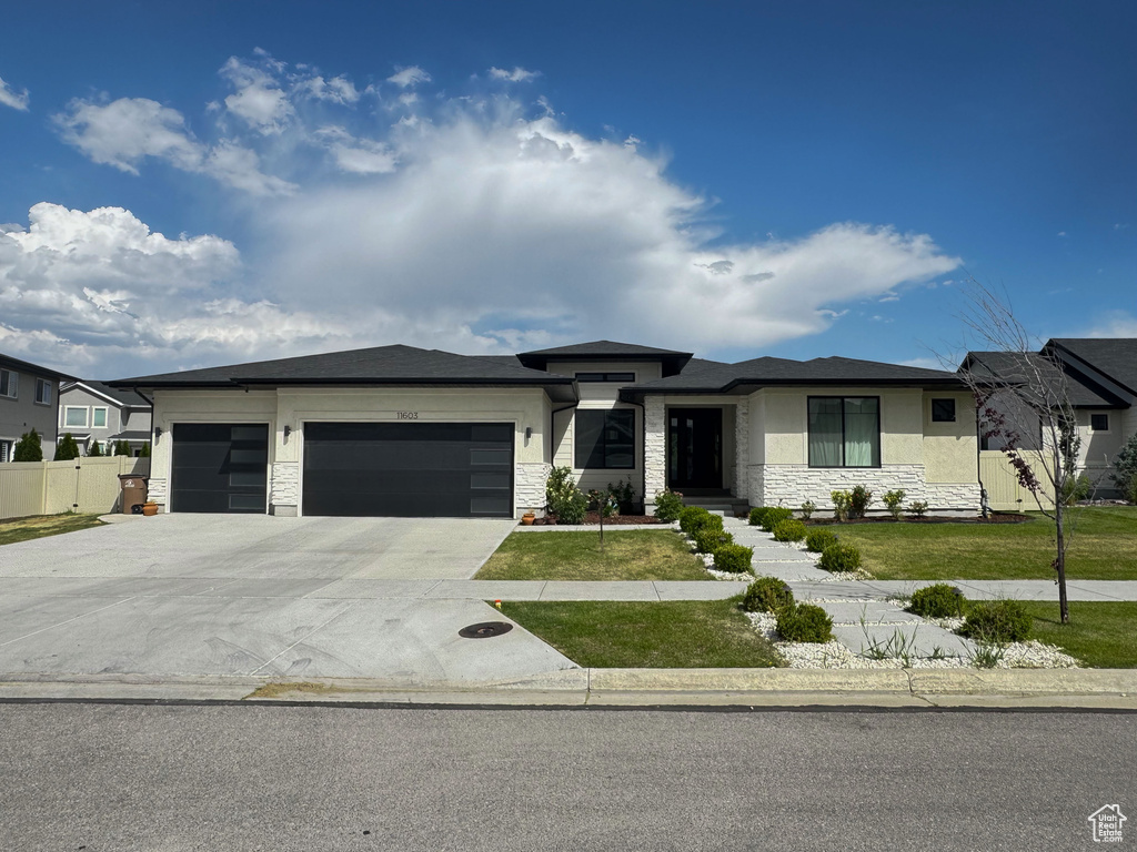 Prairie-style home featuring an attached garage, concrete driveway, stone siding, and stucco siding