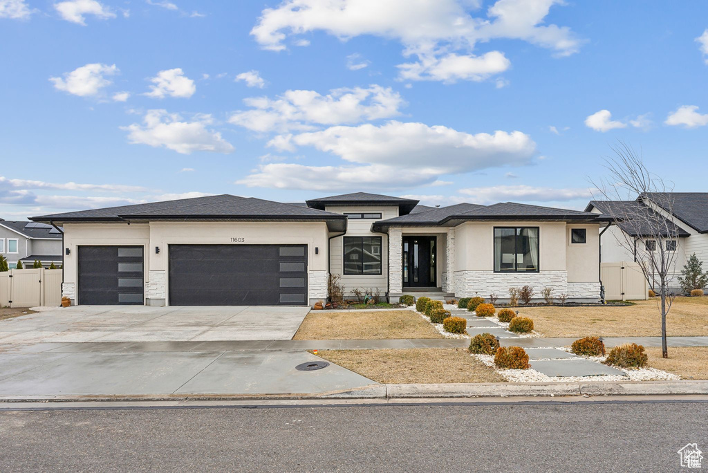 Prairie-style house with stone siding, an attached garage, driveway, a gate, and stucco siding