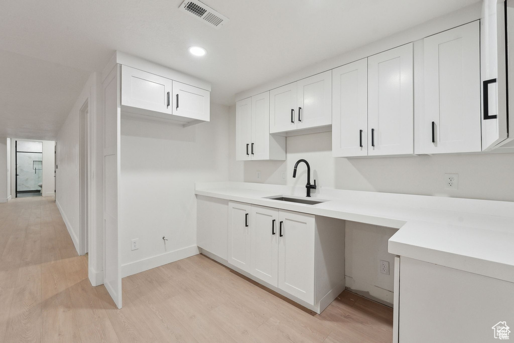 Kitchen featuring a sink, light wood-style flooring, white cabinetry, light countertops, and recessed lighting