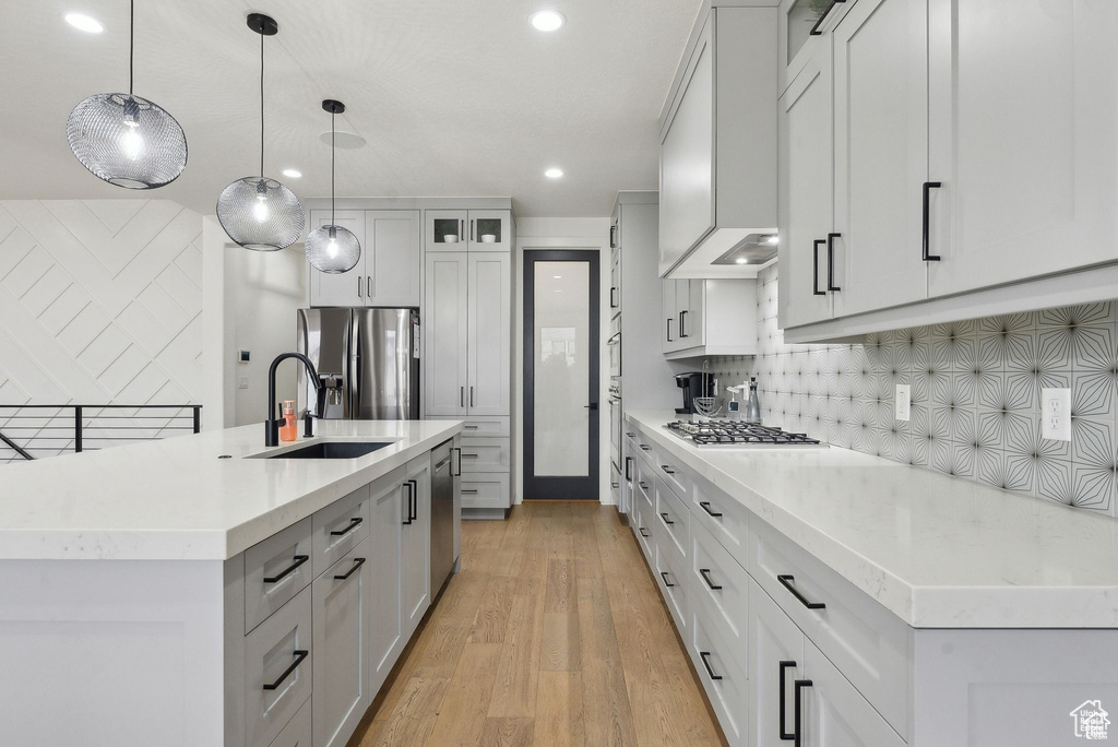 Kitchen with a sink, appliances with stainless steel finishes, light wood-style floors, tasteful backsplash, and light countertops