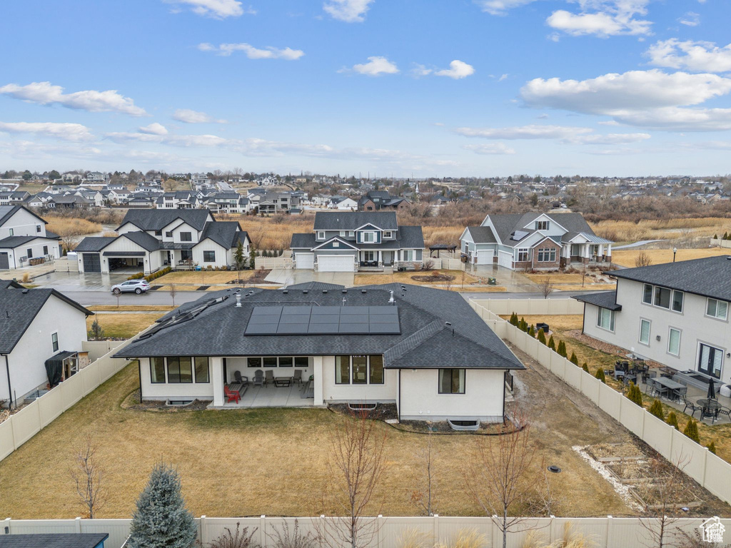 Rear view of house featuring a residential view, a fenced backyard, roof mounted solar panels, roof with shingles, and a patio