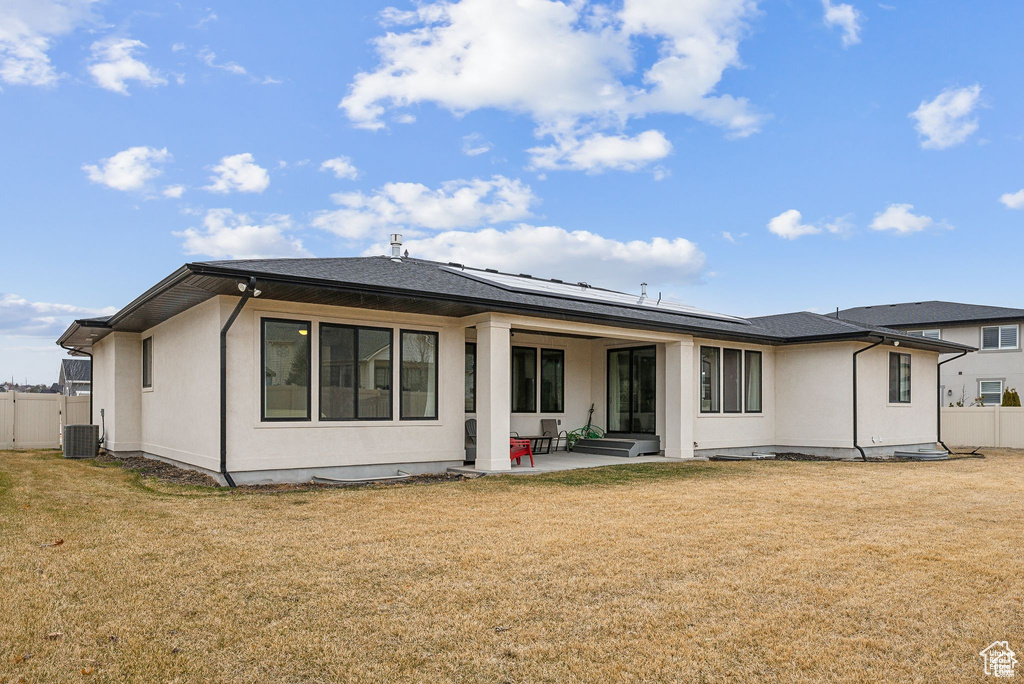 Rear view of property with a patio area, roof mounted solar panels, stucco siding, and central AC
