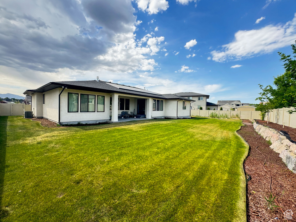 Back of house with roof mounted solar panels, a fenced backyard, and a patio area